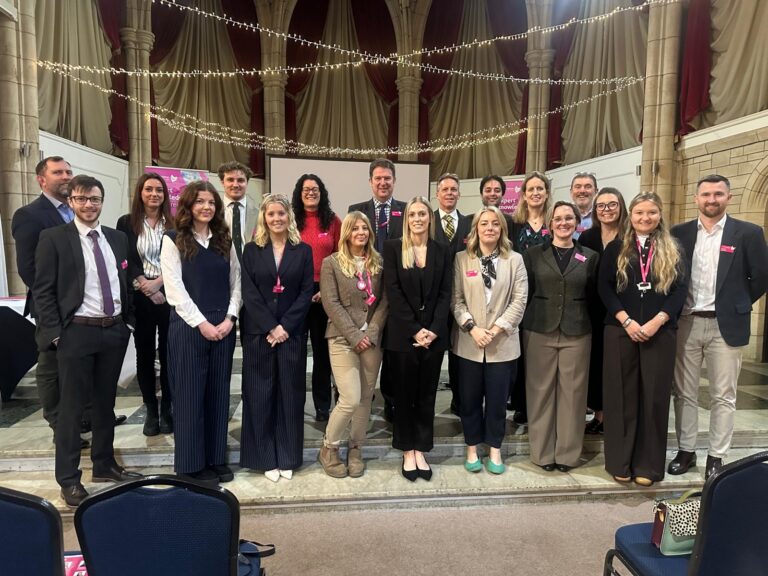 Group photo of Vickery Holman staff at an indoor networking event in a hall with stone arches and string lights.