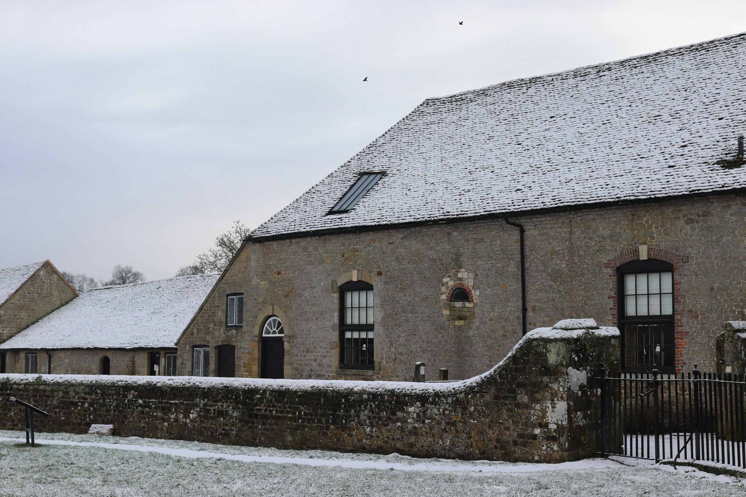 Historic stone building with a snow-covered tiled roof, traditional windows and guttering in winter.